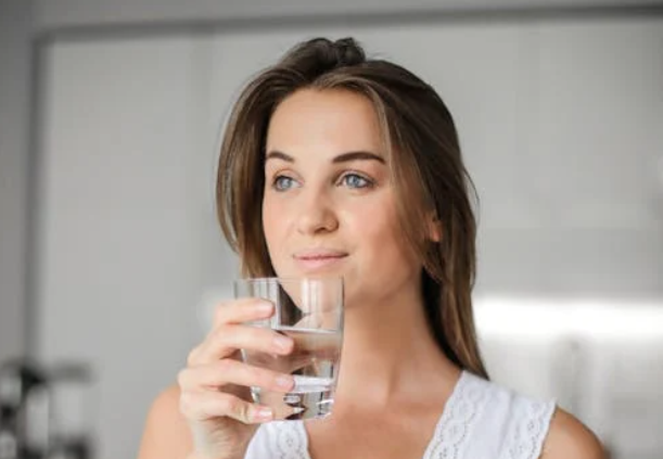 Kvinde drikker rent og sundt vand fra glas med smil.